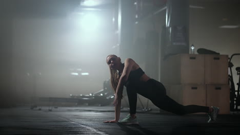 A-young-slender-woman-prepares-and-warms-up-before-training.-Hitching-and-stretching-muscles-after-a-tedious-hard-workout-in-the-dark-interior-of-the-fitness-room